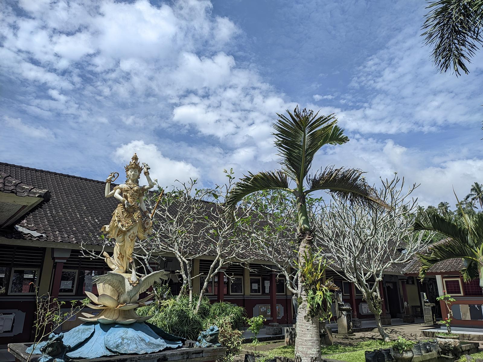 Halaman SDN 2 Duda Timur dengan patung Dewi Saraswati, pohon kamboja, dan gedung kelas beratap genteng